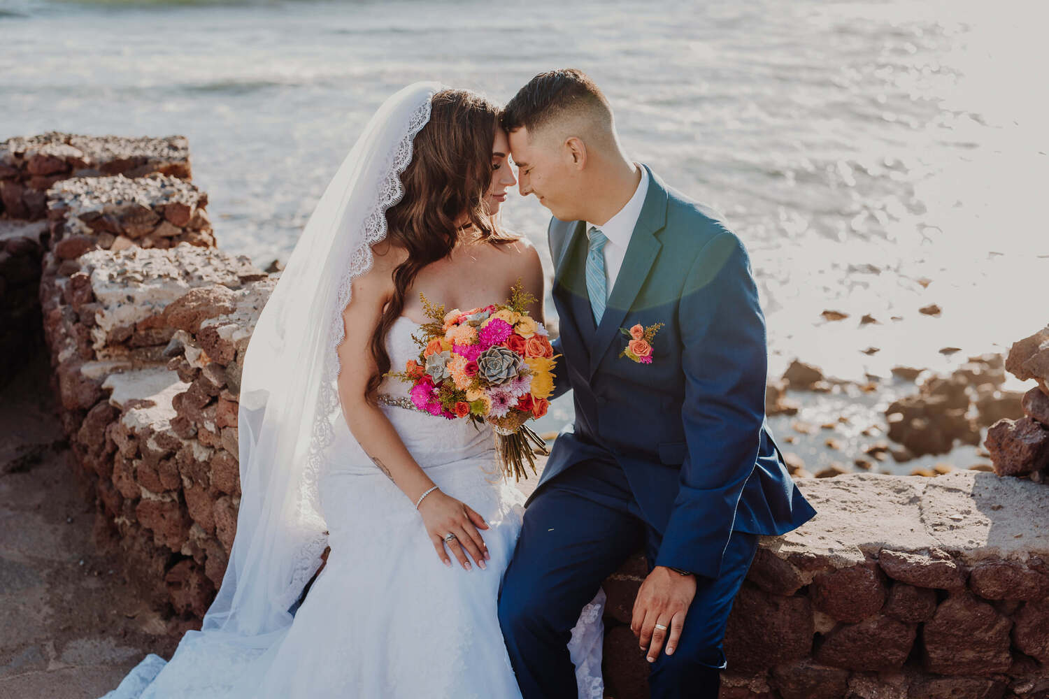 Ein Paar, das sich sehr nah vor dem Ozean bei der Hochzeit posiert.